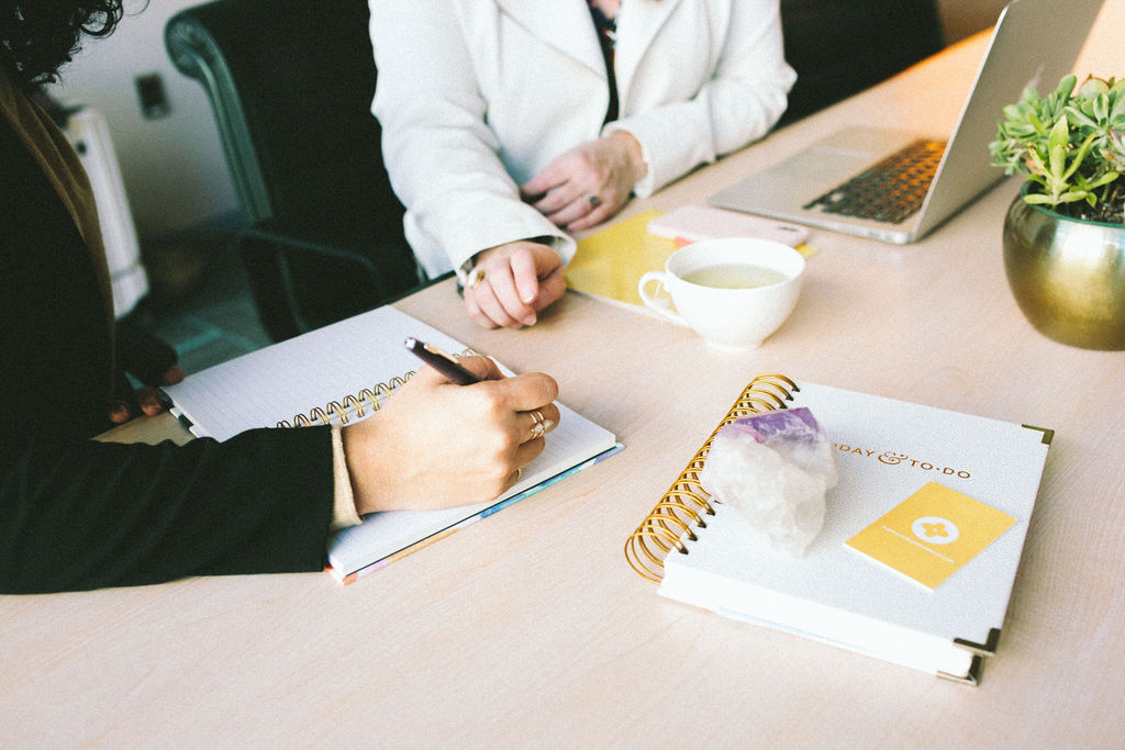 Two women at a desk only hands and table are visible