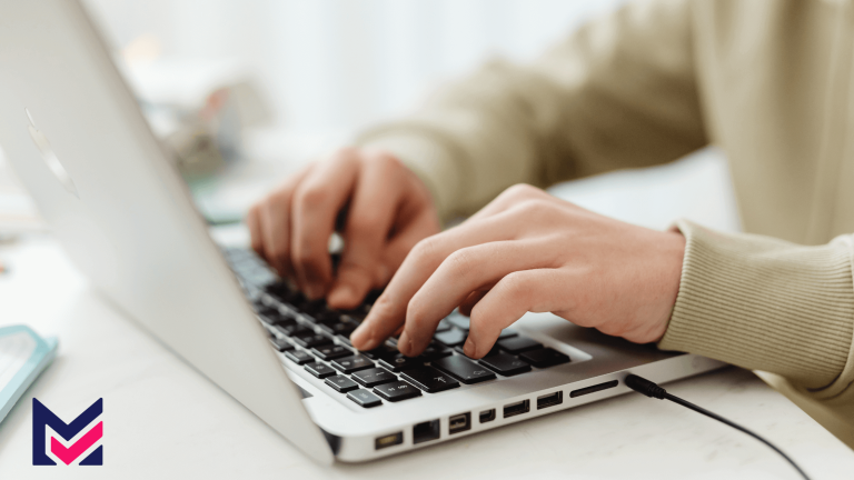 Focused shot of a woman in a sweater typing on a laptop at a desk